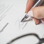 Close-up of a hand signing a contract, showcasing a pen and elegant handwriting.